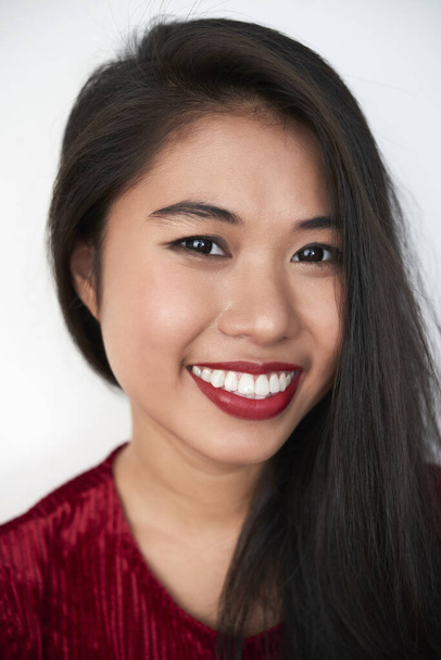 Vertical close-up studio portrait of cheerful attractive young Asian woman with dark-red lips looking at camera smiling, white background - Fotoğraf, Görsel