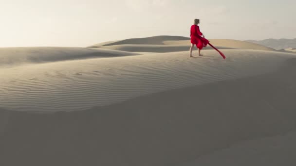 Çölde kum tepelerinin zirvesinde yürüyen bir kızın 4K hava görüntüsü. - Video, Çekim