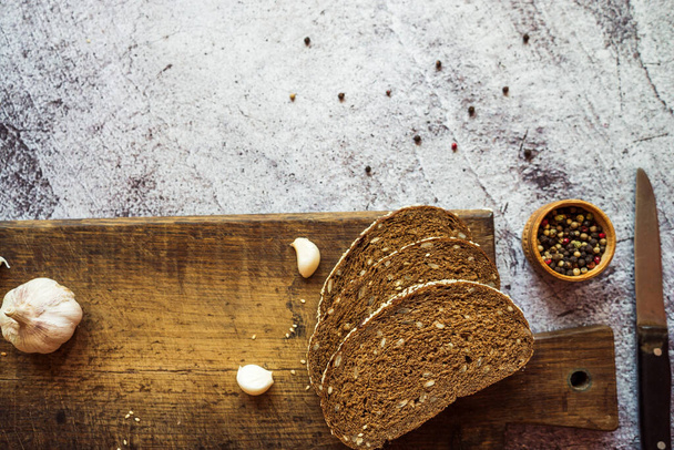 Çavdar ekmeği sarımsaklı, otlu ve baharatlı kahverengi ahşap bir tahtada gri bir zemin üzerinde - Fotoğraf, Görsel