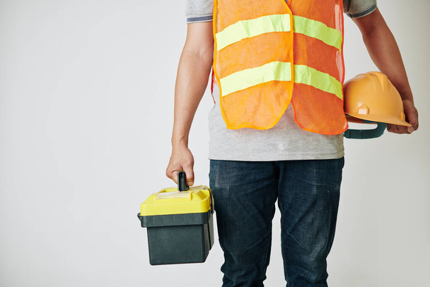 Ausgeschnittenes Bild eines Bauarbeiters mit Werkzeugkiste und Harthut in der Hand, bereit für die Arbeit - Foto, Bild