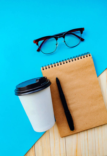 Geschäfts-, Schreibwaren- oder Bildungskonzept: Top-Bild mit leeren Seiten und einer Tasse Kaffee, Gläser auf hölzernem und blauem Hintergrund, fertig zum Hinzufügen oder Nachmachen - Foto, Bild
