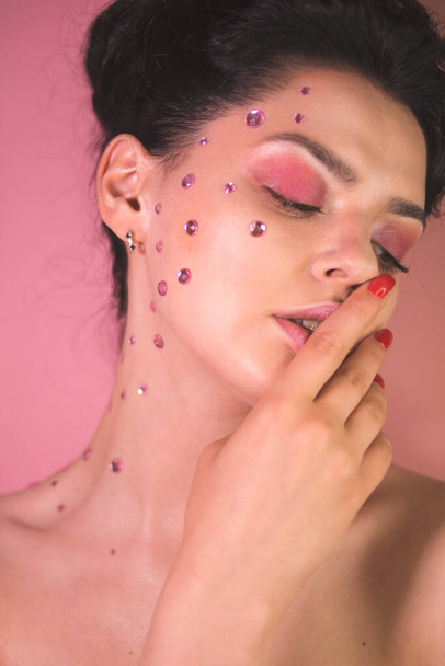 Girl with pink make-up and rhinestones on her face  on a pink background - Fotó, kép