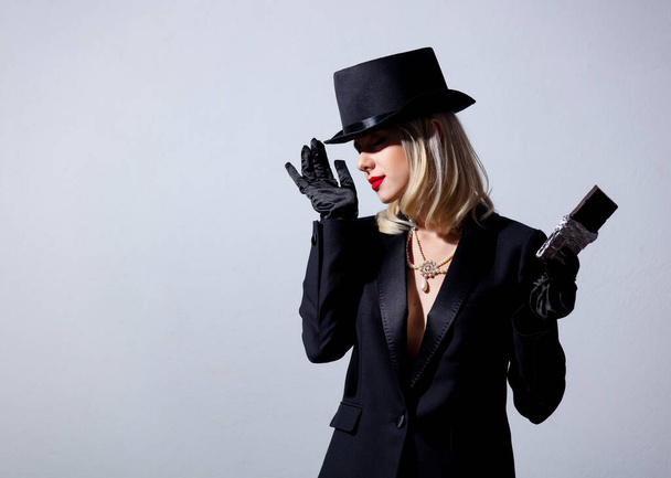 Blonde woman in vintage black jacket and top hat with chocolate bar on white background - Fotó, kép