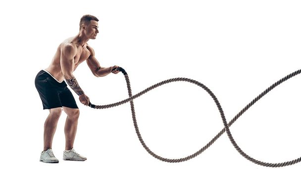 Attractive muscular man working out with heavy ropes. Photo of handsome man in sportswear isolated on white background - Фото, зображення