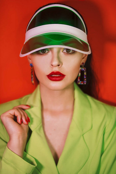 Girl in a green suit with sun visors on her head on an orange background - Foto, immagini