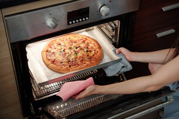 Młoda kobieta bierze tacę z gorącą świeżo upieczoną pizzą z pieca - Zdjęcie, obraz