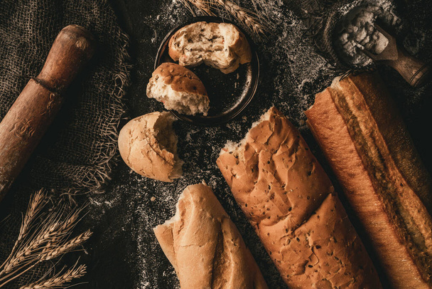 Kırık ekmek baget ekmeği, arka planda buğday filizi, çuval bezi, un. Pastanede hamur işleri ve ekmek, gıda konsepti, üst manzara. - Fotoğraf, Görsel