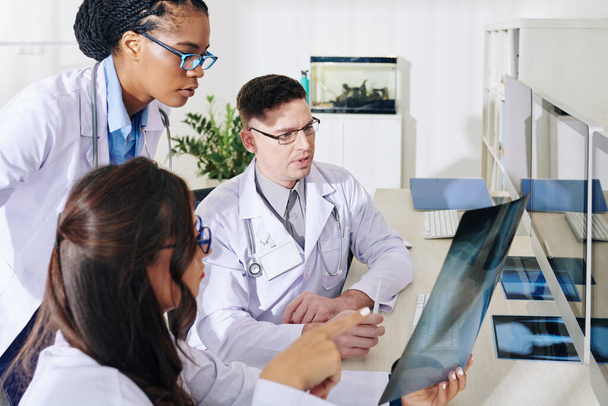 Группа обеспокоенных молодых врачей обсуждает рентген легких пациента с подозрением на COVID-19 - Фото, изображение