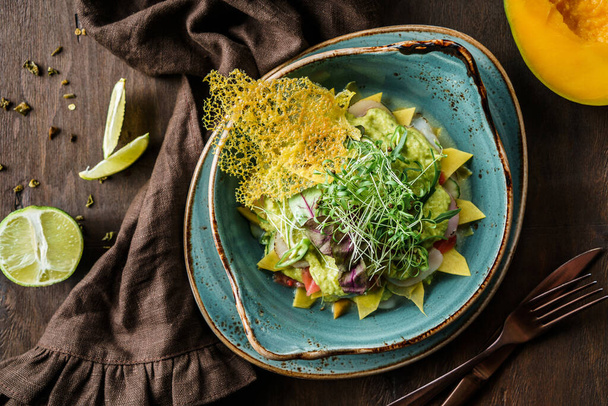 Fresh salad with sliced of turkey ham, mango, avocado, micro greens, lime in bowl on wooden background. Healthy food, dieting, top view - Photo, Image