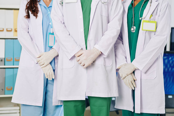 Gehakt beeld van medisch personeel in witte labjassen en rubberen handschoenen in ziekenhuishal - Foto, afbeelding