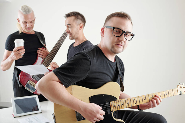 Talentierter Musiker spielt Gitarre, seine Freunde diskutieren im Hintergrund über einen neuen Song - Foto, Bild