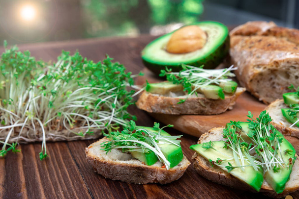 アボカドとマイクログリーンのサンドイッチは木の背景にクローズアップされています。健康的な食事。配送オプション。菜食主義だ。朝ご飯か昼ご飯か. - 写真・画像