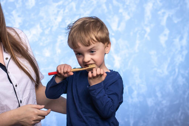 un petit enfant se tient près de maman et se brosse les dents avec une brosse à dents en bambou. articles biodégradables. enfant avec un sourire de près. concept d'hygiène, respectueux de l'environnement. place pour le texte. - Photo, image