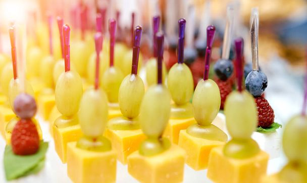 Кейтеринг. На столе сыр, виноград, черника, ежевика на шампуре
  - Фото, изображение