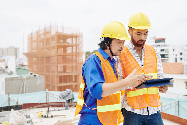 Ingénieur en chef et entrepreneur debout sur le chantier de construction et discuter du projet sur tablette - Photo, image
