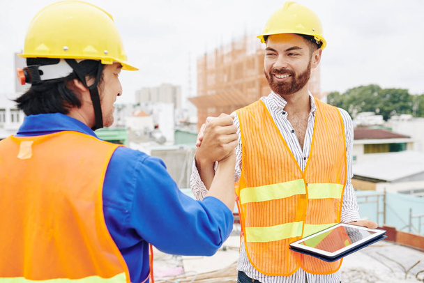 Smiling contractor with tablet computer shaking hand of builder before starting work - Photo, Image