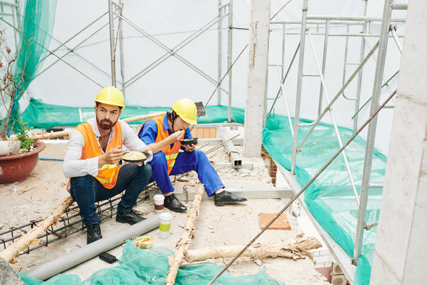 Inženýr a stavitel obědvají na staveništi, jedí nudle, salát a kávu - Fotografie, Obrázek