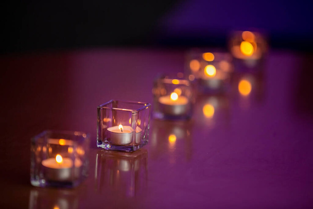 Lit theelichtkaarsen in glazen containers op een glanzend tafelblad met een paarse tint achtergrond - Foto, afbeelding