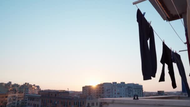 Βρεγμένα ρούχα που κρέμονται στο μπαλκόνι στο φόντο του καταπληκτικού ηλιοβασιλέματος της πόλης. Μαλακό στέγνωμα αέρα καθαρά πλυντήρια πλυμένα με απορρυπαντικό στο πλυντήριο. Στεγνώματα ρούχων σε εξωτερικούς χώρους - Πλάνα, βίντεο