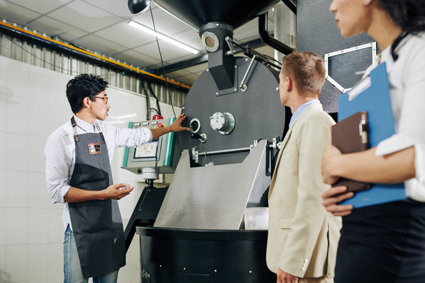検査官に彼の近代的なコーヒー焙煎所で機器を示す起業家 - 写真・画像
