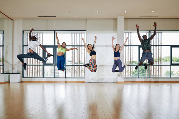 Energické nadšení mladí lidé skákání do vzduchu v prostorném tanečním sále po tréninku - Fotografie, Obrázek