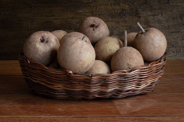Fruta de la sapotis expuesta en cesta en fondo de madera rústica
 - Foto, Imagen