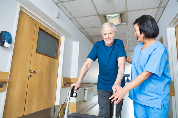 Asiatische Krankenschwester hilft älterem Mann mit Rollator auf dem Krankenhausboden. - Foto, Bild