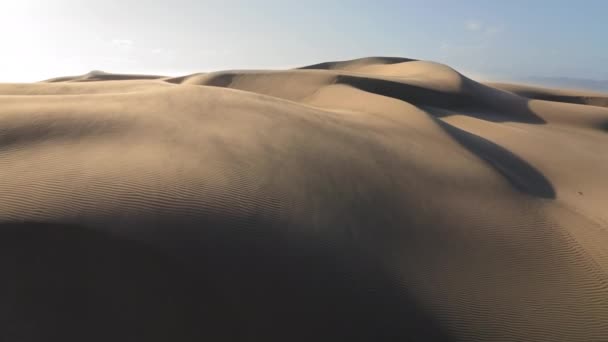 4K aerea sul vento soffiando la sabbia fuori dalla cima delle dune ondulate di sabbia dorata - Filmati, video