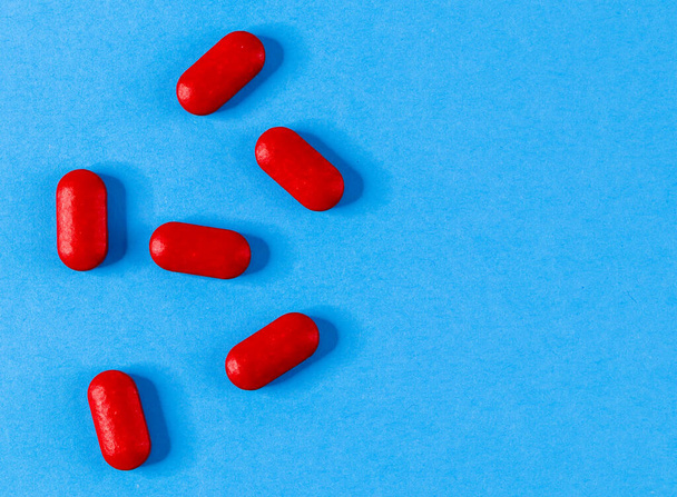 Seis píldoras rojas se dispersan a la izquierda sobre un fondo azul y con espacio para el texto a la derecha, vista superior de cerca
. - Foto, Imagen