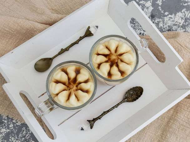 Een koffiedessert in glazen mokken met dessertlepels op een houten plank ligt op het materiaal, close-up bovenaanzicht. - Foto, afbeelding