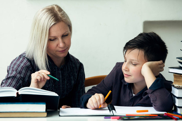 Schoolboy and tutor sits at a table does homework. - Foto, Bild