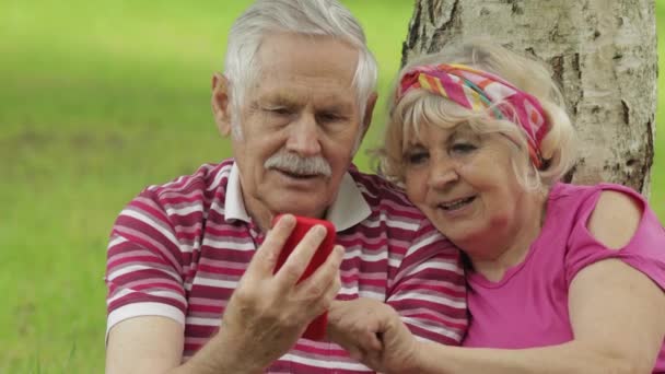 Pique-nique familial. Vieux grands-parents âgés couple dans le parc en utilisant smartphone navigation en ligne, achats - Séquence, vidéo