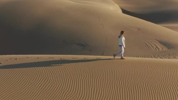 4K slow motion antena kobiety przechodzącej przez wydmy z pięknym wzorem falistym - Materiał filmowy, wideo