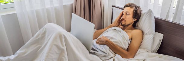 Man patiënt is ziek terwijl liggend in zijn bed en roept een online arts door middel van een gadget BANNER, LANG FORMAT - Foto, afbeelding