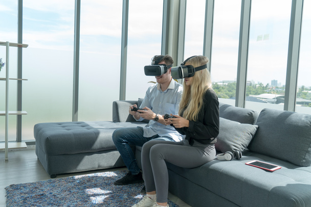 Beyaz tenli genç çift, eğlence için evlerindeki oturma odasında sanal gerçeklik gözlükleriyle video oyunu oynamaktan zevk alıyorlar.. - Fotoğraf, Görsel