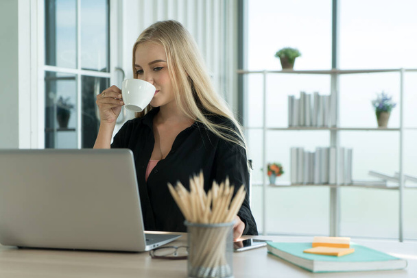 joven mujer de negocios estudiante freelancer beber café mientras trabaja en computadora portátil portátil haciendo investigación en el escritorio de la oficina en casa
. - Foto, imagen