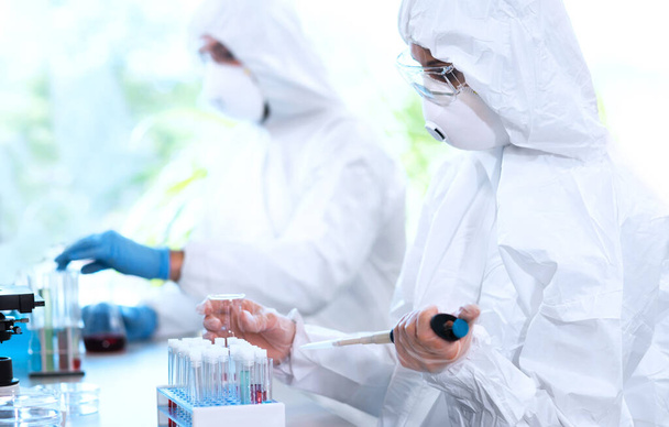研究室で働く保護スーツやマスクの科学者は、顕微鏡、試験管などの実験装置を使用しています。生物学的危険性、医薬品の発見、細菌学とウイルス学の概念. - 写真・画像