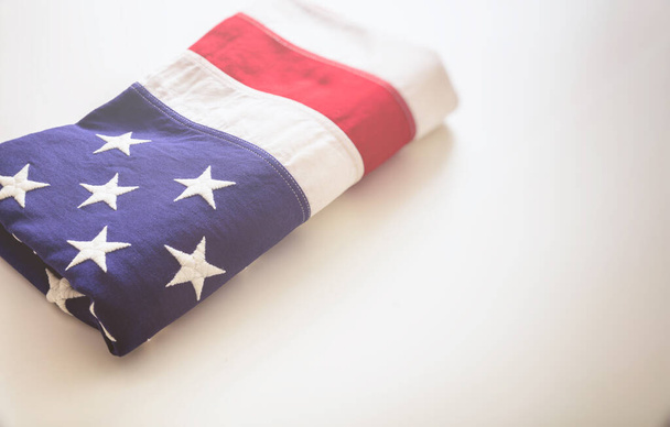 Флаг США сложен на белом фоне. Вид американского флага крупным планом, скопируйте пространство. День памяти и 4 июля, концепция Дня Независимости. Карточка, шаблон постера
 - Фото, изображение
