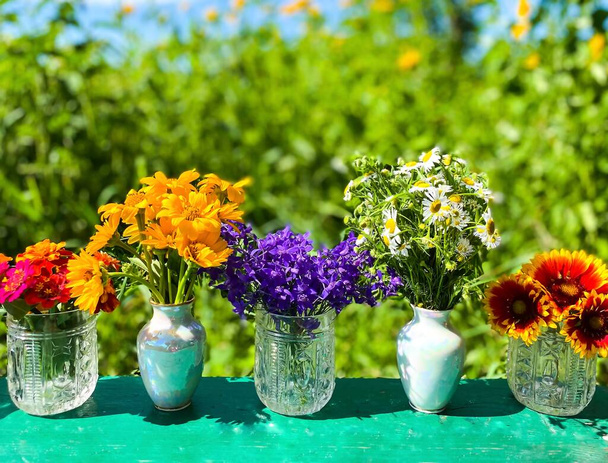 Boeketten van kleurrijke wilde bloemen in decoratieve vazen. Defocus lichte achtergrond. - Foto, afbeelding