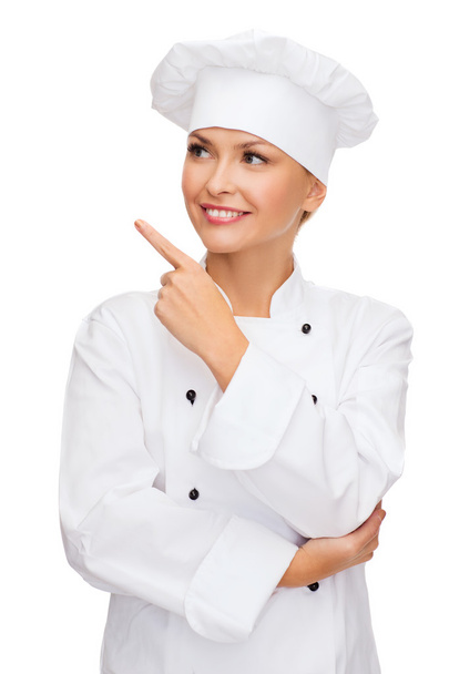 Smiling female chef pointing finger to sonething - Foto, Bild