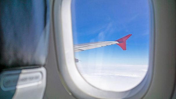 Вид на небо с прозрачного стеклянного сиденья на крыло самолета, путешествующего по облакам и яркому голубому небу - Фото, изображение