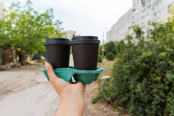 街の背景がぼやけて手にコーヒーの2つのガラス。使い捨てカップでテイクアウトコーヒー。軽食だよ。朝のコーヒー通り. - 写真・画像