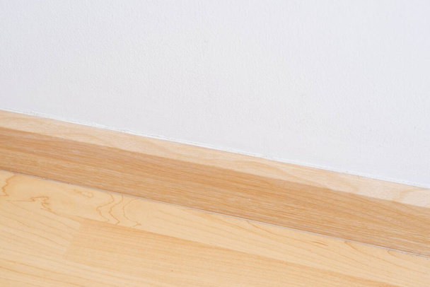 Zócalo de base de pared de madera, material de acabado con suelo laminado de madera y pared de mortero blanco. Habitación vacía con pared blanca y suelo de madera nuevo diseño moderno y limpio
. - Foto, Imagen