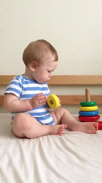 Малыш играет на кровати с деревянной игрушечной пирамидой
 - Кадры, видео
