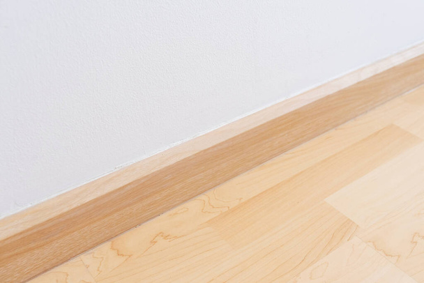 Fából készült fali szegélyléc, fa padlóval és fehér habarcsfallal. Üres szoba fehér fallal és fapadlóval. - Fotó, kép