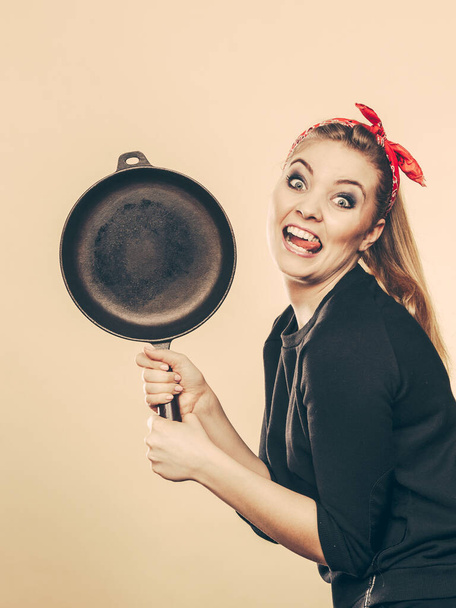 Alegría y diversión durante la preparación de alimentos. Mujer rubia sonriente en estilo retro divirtiéndose en la cocina. Chica juguetona con accesorios de cocina
. - Foto, Imagen