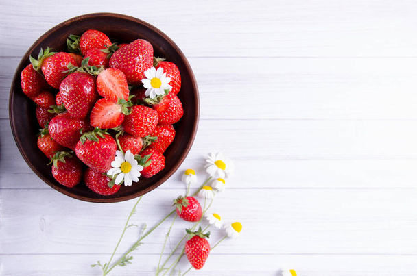 Ripe fresh strawberries in a clay bowl with camomile flowers, rustic background - 写真・画像