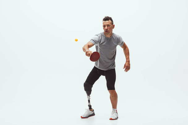 Athlete with disabilities or amputee isolated on white studio background. Professional male table tennis player with leg prosthesis training and practicing in studio. - Φωτογραφία, εικόνα