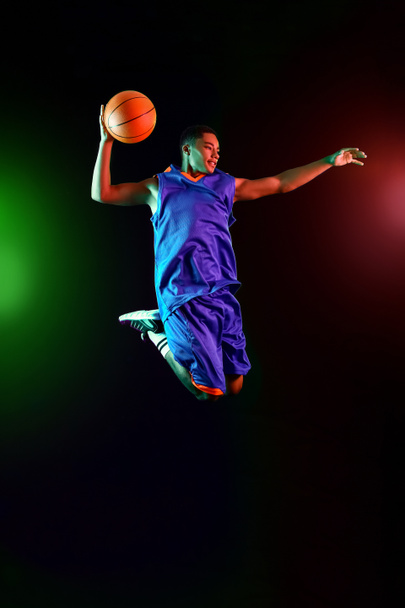 Young jumping African-American basketball player on dark background - Fotoğraf, Görsel