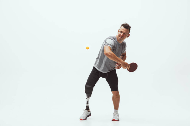 Athlete with disabilities or amputee isolated on white studio background. Professional male table tennis player with leg prosthesis training and practicing in studio. - Photo, image